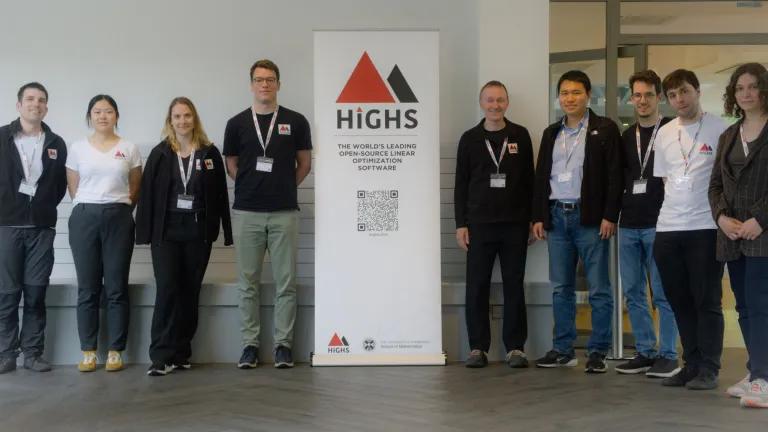 The HiGHS team and workshop speakers stand in a row surrounding a roller banner showing the HiGHS logo (a red and black triangle).