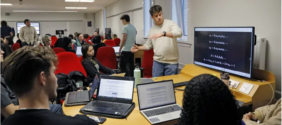 Students grouped around presenting monitor with laptops 