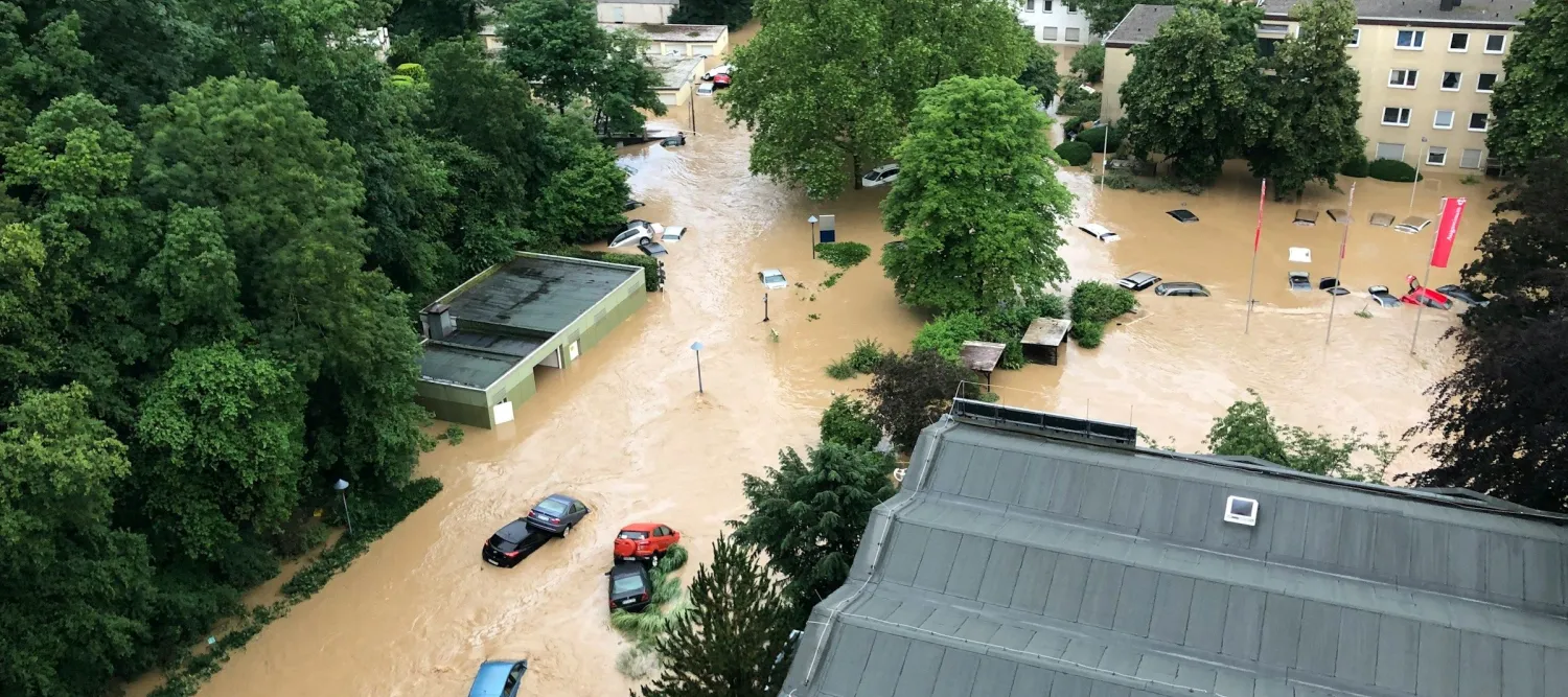 An aerial view of cars floating in brown floodwater between buildings 