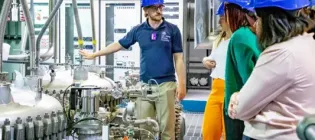 A group is touring a nuclear power facility wearing blue hard hats