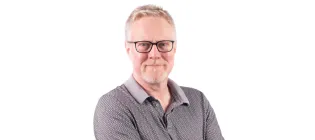 A professional headshot of Des with his arms folded