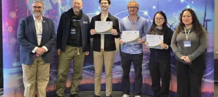 A photo of the inning team and judges. They are standing in a line while holding up their certificates.