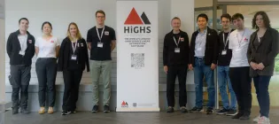 The HiGHS team and workshop speakers stand in a row surrounding a roller banner showing the HiGHS logo (a red and black triangle).