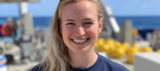 A photo of Lois aboard a research vessel on a sunny day. She is wearing a dark blue t-shirt and has sunglasses on her head.