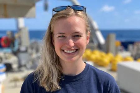A photo of Lois aboard a research vessel on a sunny day. She is wearing a dark blue t-shirt and has sunglasses on her head.