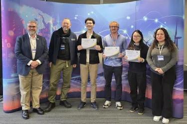 A photo of the inning team and judges. They are standing in a line while holding up their certificates.
