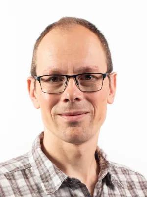 A professional headshot of David Siska. He's looking at the camera and wearing a checked shirt and black wire-rimmed glasses.