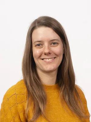 A professional headshot of Amy wearing a yellow jumper and looking direct to camera